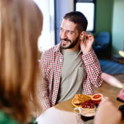 Smiling man wearing audio aids while sitting at the kitchen table and talking with his family and friends