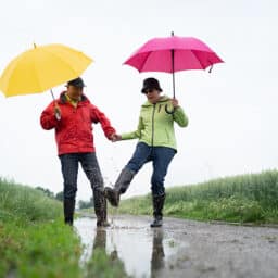 Senior couple with umbrellas jumping in a puddle.