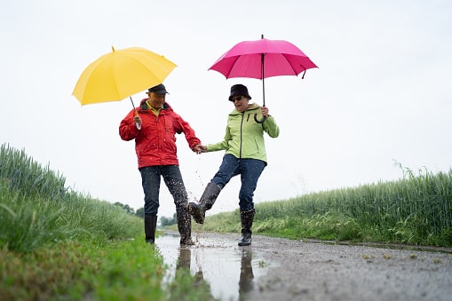 Senior couple with umbrellas jumping in a puddle.